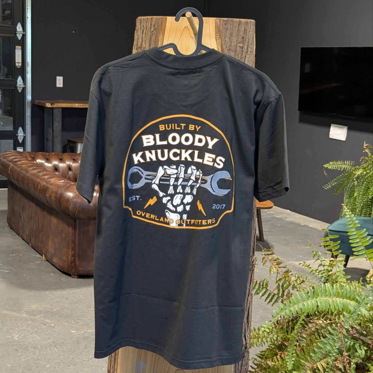 Back side of tee hanging on a wooden stand showing skeleton hand holding wrench