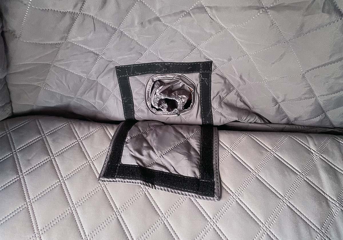 Close-up of quilted fabric with a square cutout and rolled-up object inside.