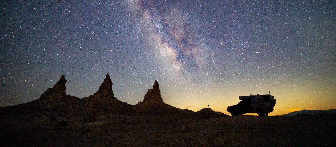 Desert landscape with silhouetted vehicle under a starry sky with the Milky Way.