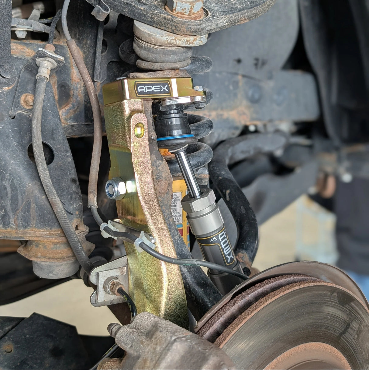 Close-up of a vehicle suspension system with Apex and Lukx branding.