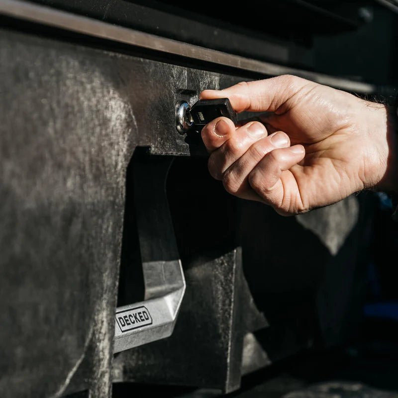 Hand inserting a key into a vehicle's ignition, with 'DECKED' branding visible on the door panel.