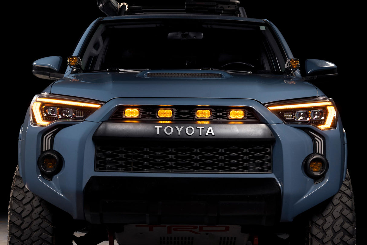 Front view of a Toyota vehicle with illuminated headlights on a black background