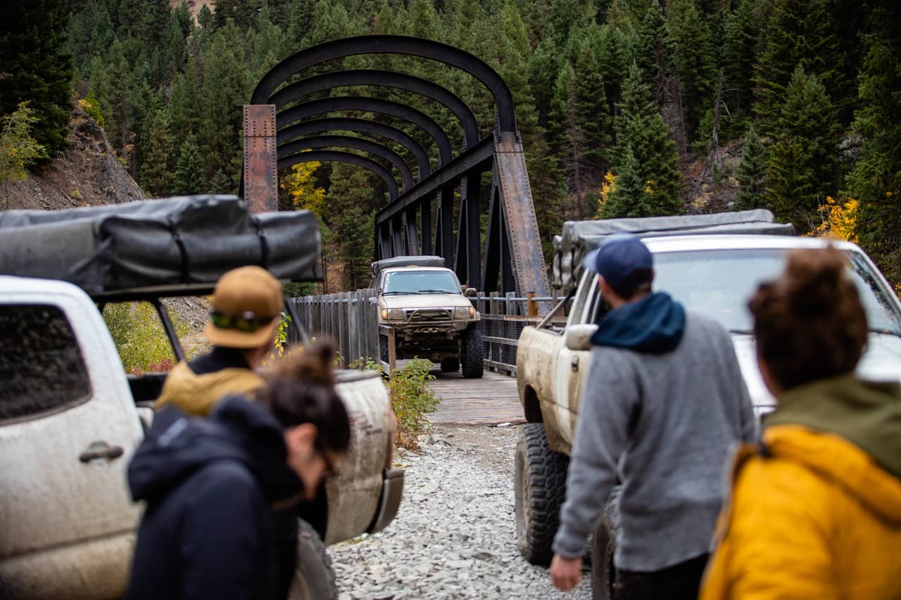 Group of people walking towards a bridge with off-road vehicles in a forested area