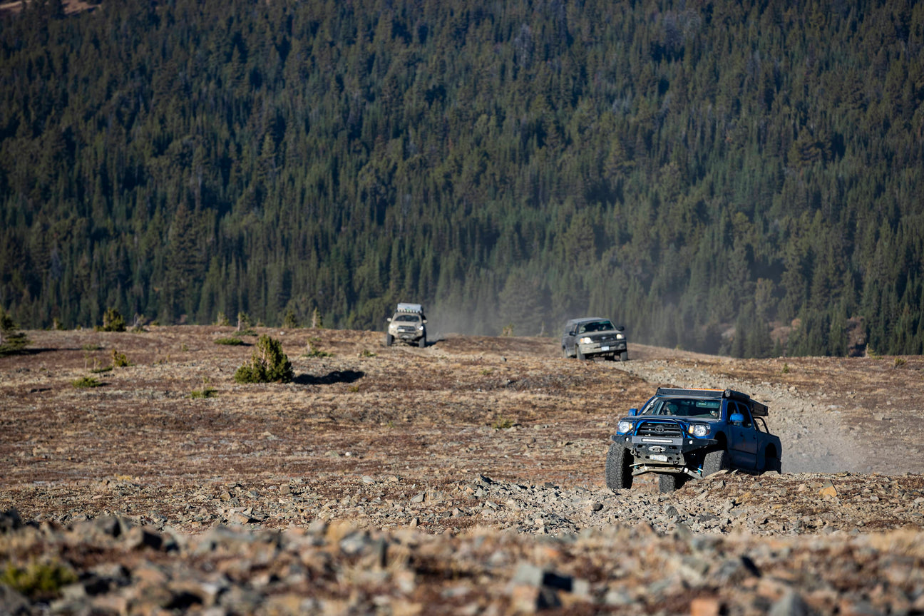 3 trucks driving off road with a forest in the background
