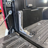 A close-up of a black metal truck bed accessory bracket mounted on the side of a truck bed, with a textured black liner floor and tailgate visible.