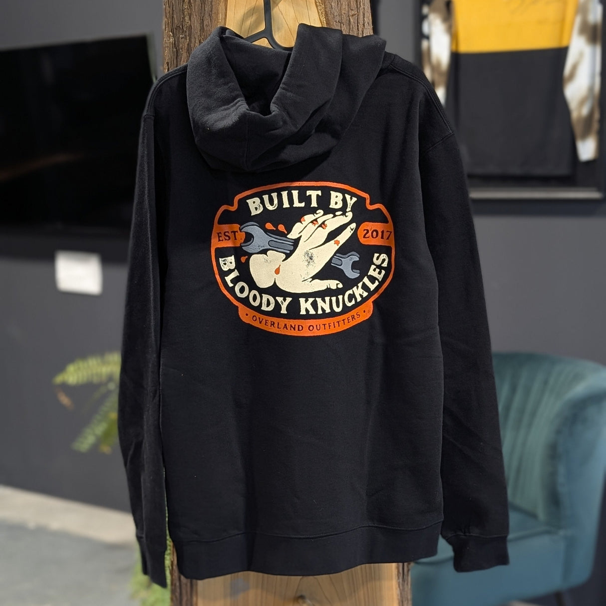 Black hoodie with a design and the text 'built by bloody knuckles' on a wooden stand in an indoor setting