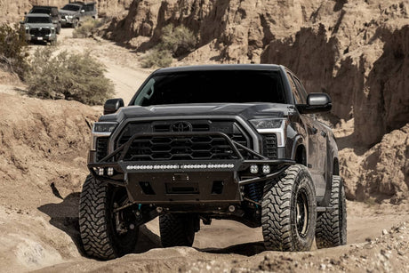Black off-road truck driving on a dirt road with rocky cliffs in the background