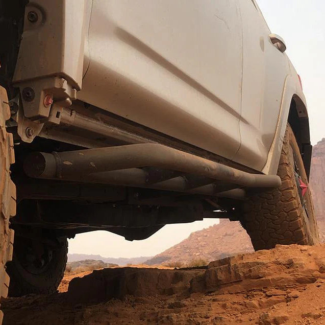 Close-up of an off-road vehicle climbing a rocky terrain with a desert landscape in the background.