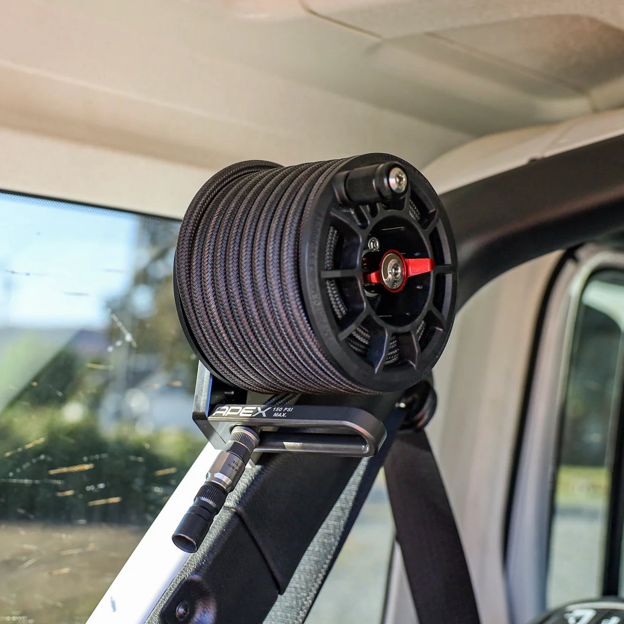 Carabiner with a compressor hose reel attached to a car's interior, with a blurred outdoor background.