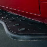 Close-up of a black metal vehicle side step running board mounted beneath a red car body panel.