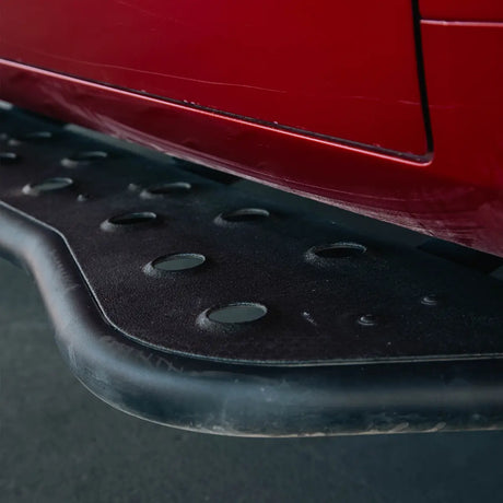 Close-up of a black metal vehicle side step running board mounted beneath a red car body panel.