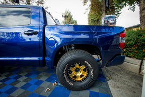 Blue truck with a tire on a checkered floor outdoors