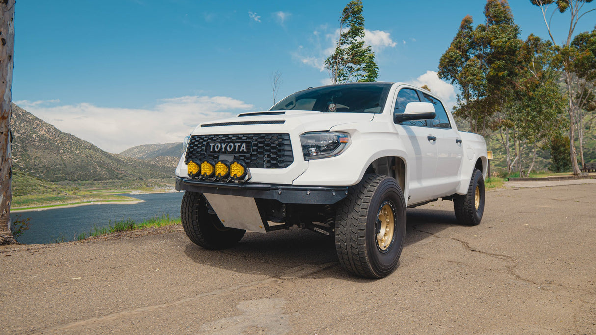 White Toyota truck parked on a road with a scenic background of trees and mountains.
