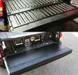 A black plastic tailgate insert for a Toyota Tacoma, displayed in an installed position on the truck's bed.
