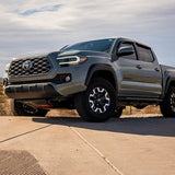 Gray Tacoma truck parked on a concrete surface with a cloudy sky in the background with white fog lights