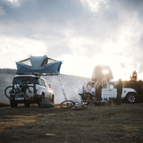 Two vehicles with rooftop tents in a natural setting with people around.
