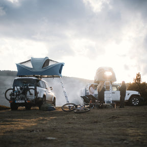 Two vehicles with rooftop tents in a natural setting with people around.