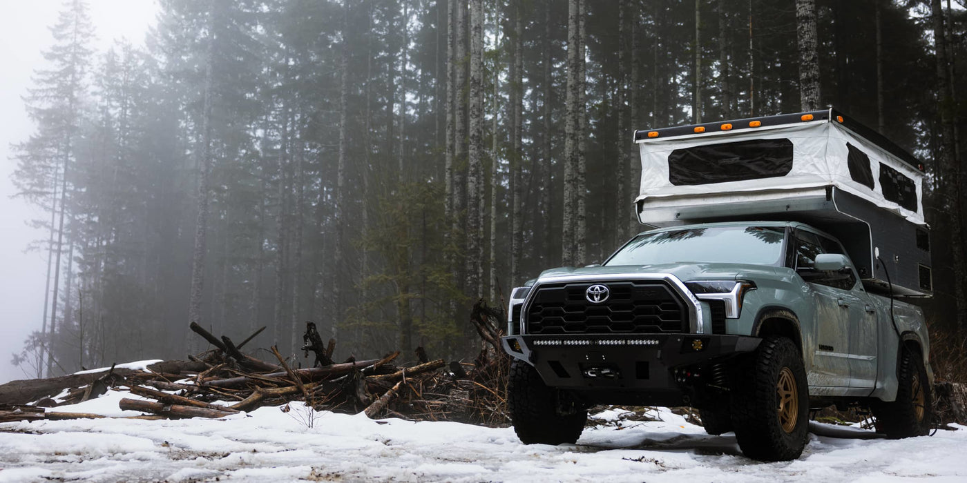 Toyota truck with a camper shell parked in a snowy forest