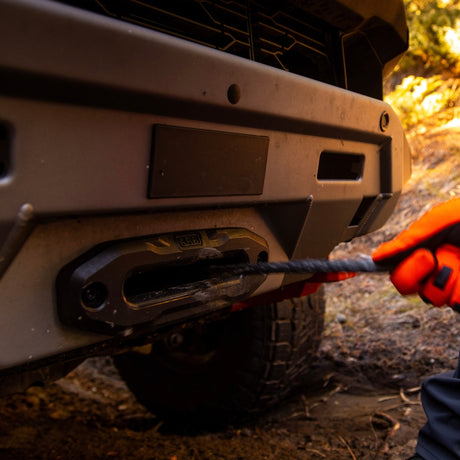 Person using a rope to pull a vehicle's bumper, with a focus on the action and equipment.