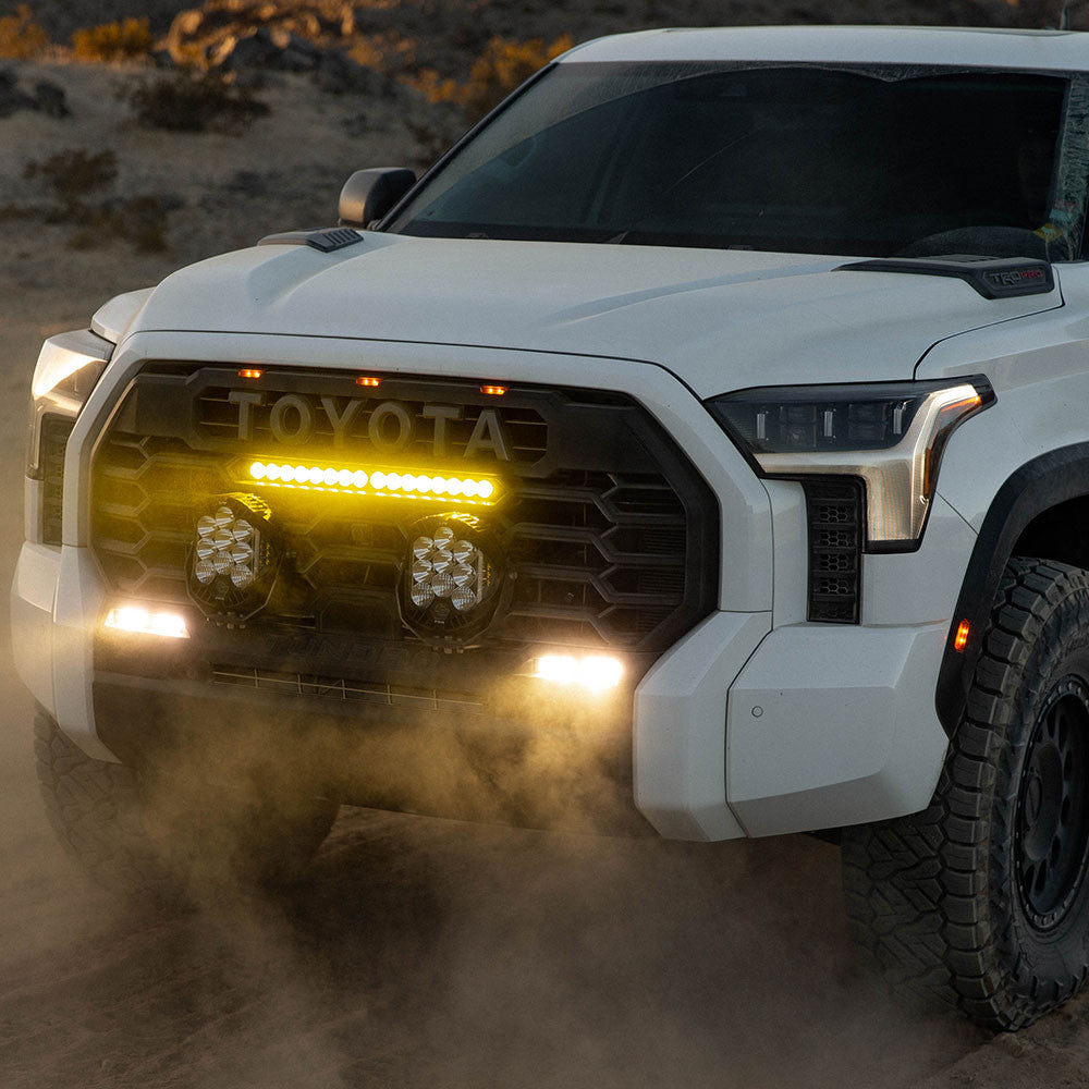 White Toyota truck driving on a dirt road with dust in the foreground