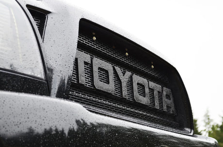 Close-up of a Toyota logo on a vehicle grille with raindrops.