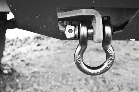 Metal shackle attached to a vehicle's hitch receiver on a gravel surface