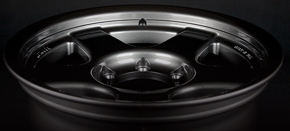 Face 2. Close-up of a black alloy wheel on a dark background
