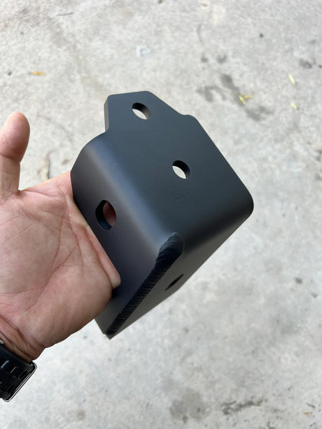 Black metal bracket held in a hand against a concrete floor background