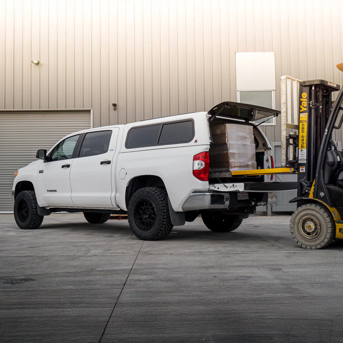 White pickup truck with an open cargo area next to a forklift in an industrial setting