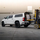 White pickup truck with an open cargo area next to a forklift in an industrial setting