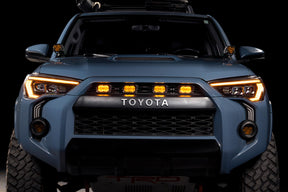 Front view of a Toyota vehicle with illuminated headlights on a black background