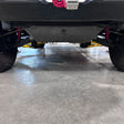 A close-up, low-angle view of a vehicle's undercarriage, showing a brushed metal skid plate on a concrete floor inside a garage.