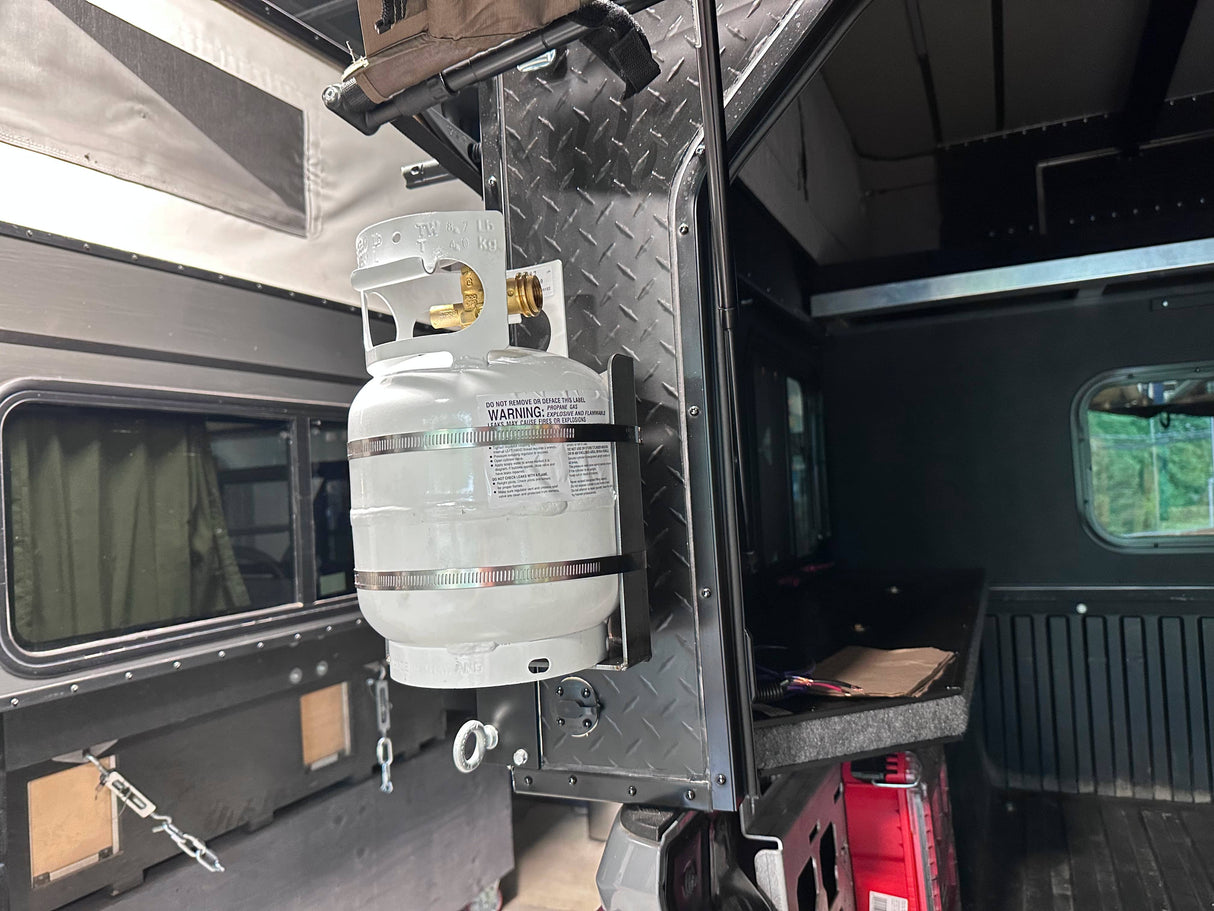 Propane tank secured in a bracket mounted to the back of a truck bed camper.