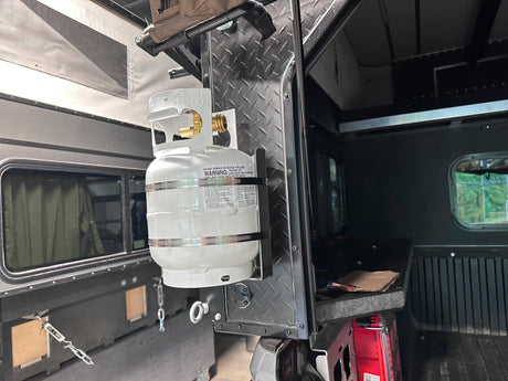Propane tank secured in a bracket mounted to the back of a truck bed camper.