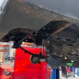 Close-up of a vehicle's undercarriage with a red car in the background.