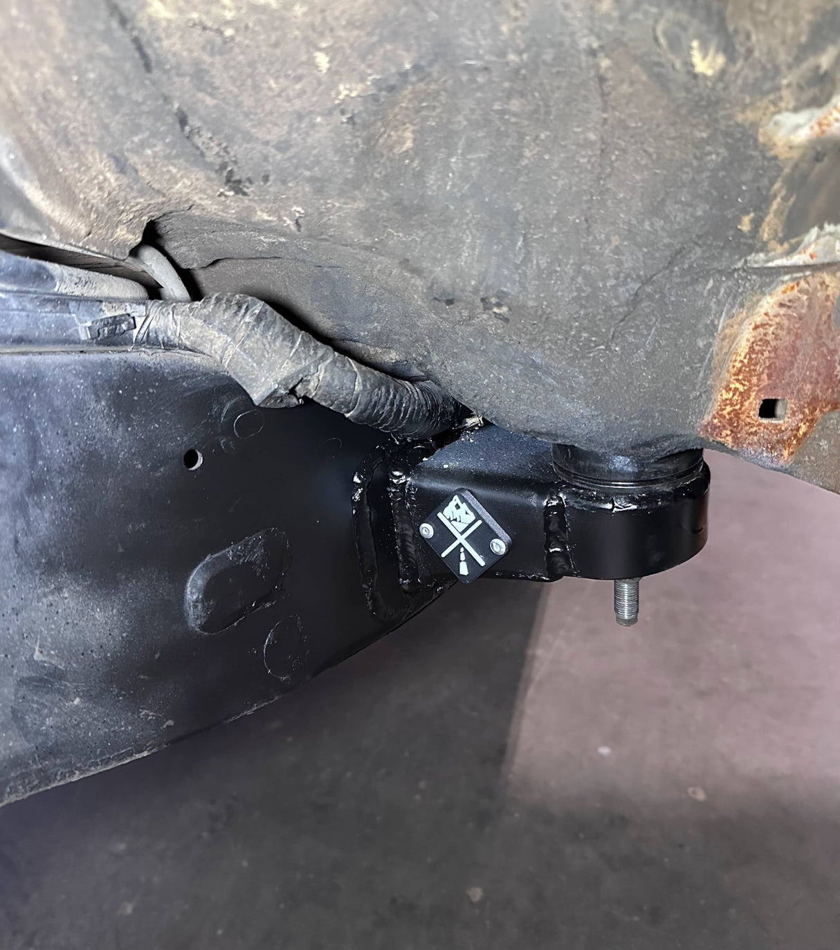 Close-up of a black metal bracket attached to a vehicle's undercarriage with visible rust.