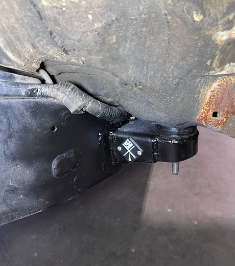 Close-up of a black metal bracket attached to a vehicle's undercarriage with visible rust.