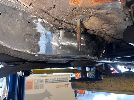 Close-up of a car's undercarriage with visible rust and mechanical components.