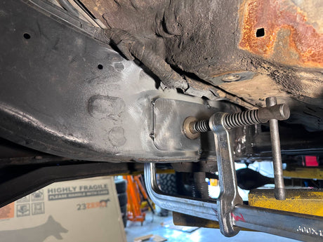Close-up of a vehicle's undercarriage with a clamp on a workshop floor.