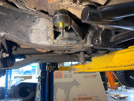 Close-up of a car suspension system with a yellow jack stand in a garage setting.