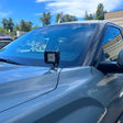 A ditch light attached to the hood of a truck parked outside of a warehouse on a clear day.