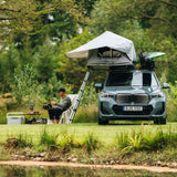 Person sitting by a car with a rooftop tent in a natural setting