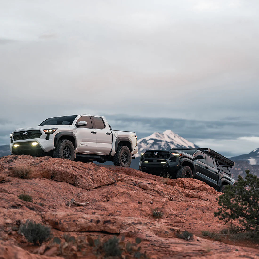 Two Toyota trucks on a rocky outcrop with mountains in the background