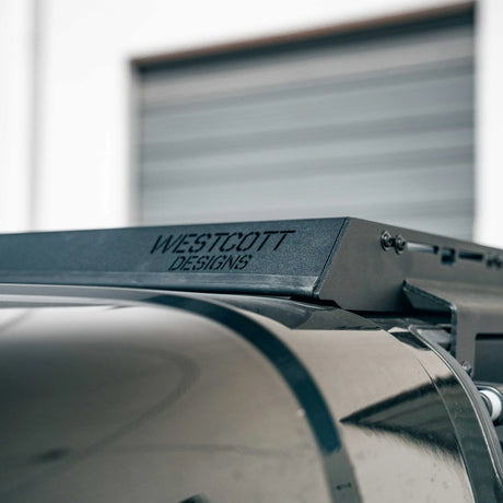 Close-up of a black metal mounting bracket with the brand name 'WESTCOTT DESIGNS' engraved on its side, positioned above a dark curved surface.