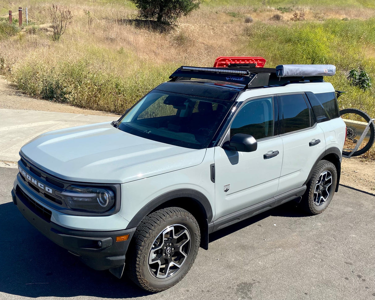 Light blue SUV with roof rack and bike on a paved road with grassy area in the background