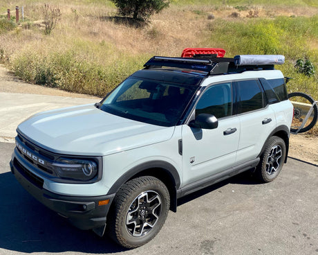 Light blue SUV with roof rack and bike on a paved road with grassy area in the background