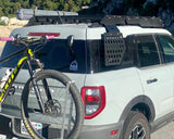 White SUV with a bike attached to its rear, parked outdoors with trees in the background